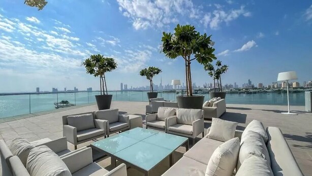 A rooftop terrace with outdoor seating, large potted plants, and a view of the city skyline across the water. - Aya - Outstanding 1BR Apartment With Amazing Creek Views (Dubai)
