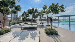 A rooftop pool area with lounge chairs, palm trees, and a view of the city skyline. - Aya - Outstanding 1BR Apartment With Amazing Creek Views (Dubai)