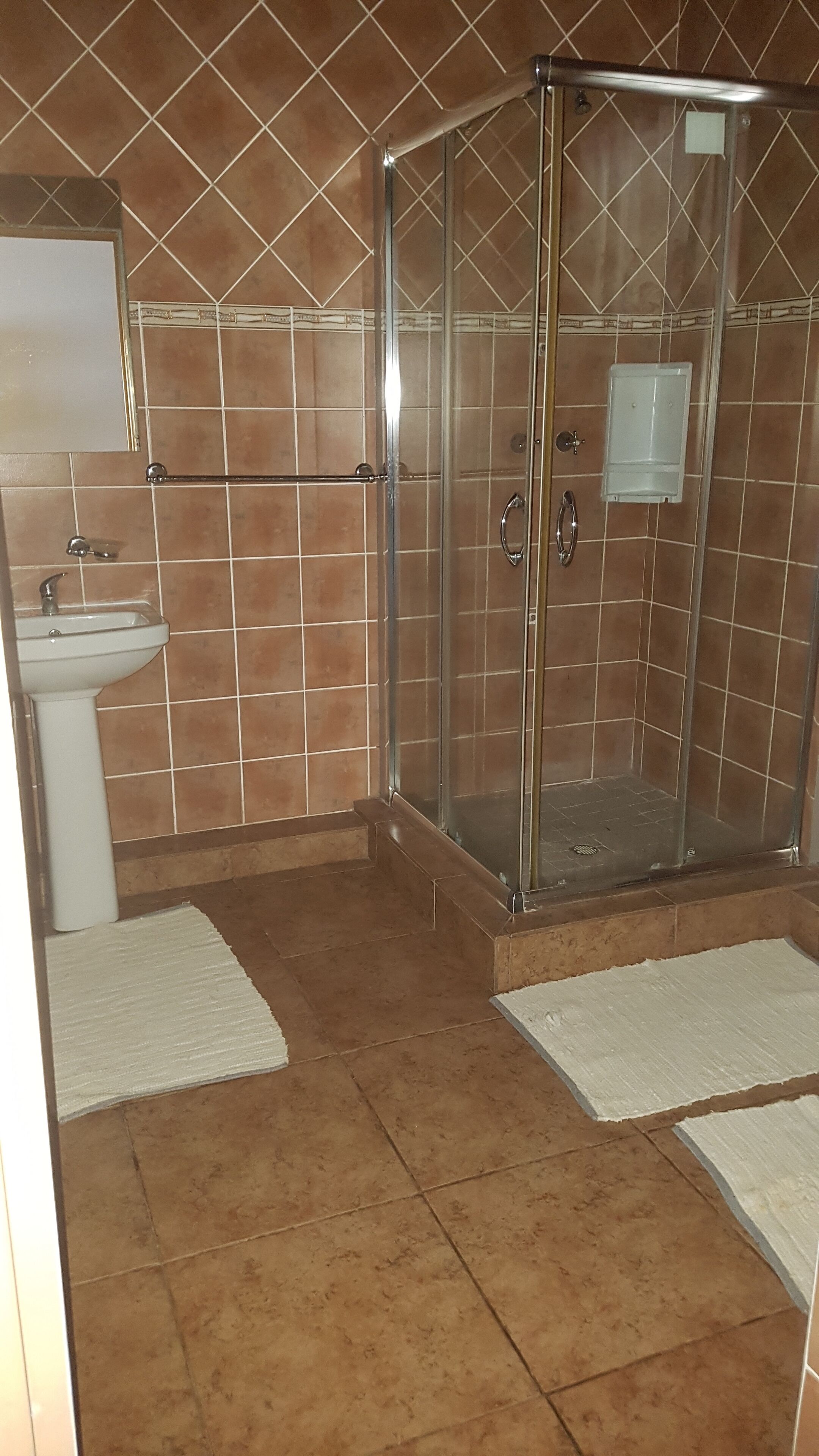 A bathroom with a glass-enclosed shower, a sink, and a tiled floor.