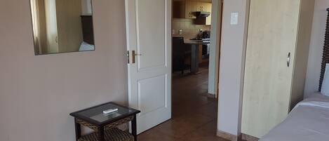 A hotel room with a bed, a small table, a mirror, and a view into the kitchen area.