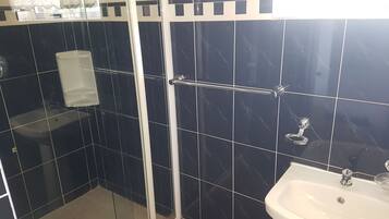 Um banheiro com paredes revestidas de azulejos escuros, uma pia branca e um box de vidro.