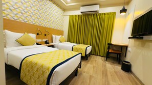 A hotel room with two beds, a desk, a chair, an air conditioning unit, a television, and a patterned wall. - Regenta Inn Bannerghatta Bangalore (Bengaluru)
