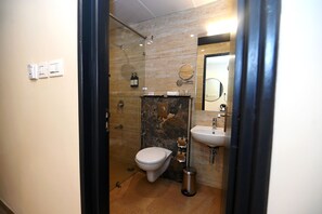 A modern bathroom with a glass-enclosed shower, a toilet, a sink, and a mirror. - Regenta Inn Bannerghatta Bangalore (Bengaluru)