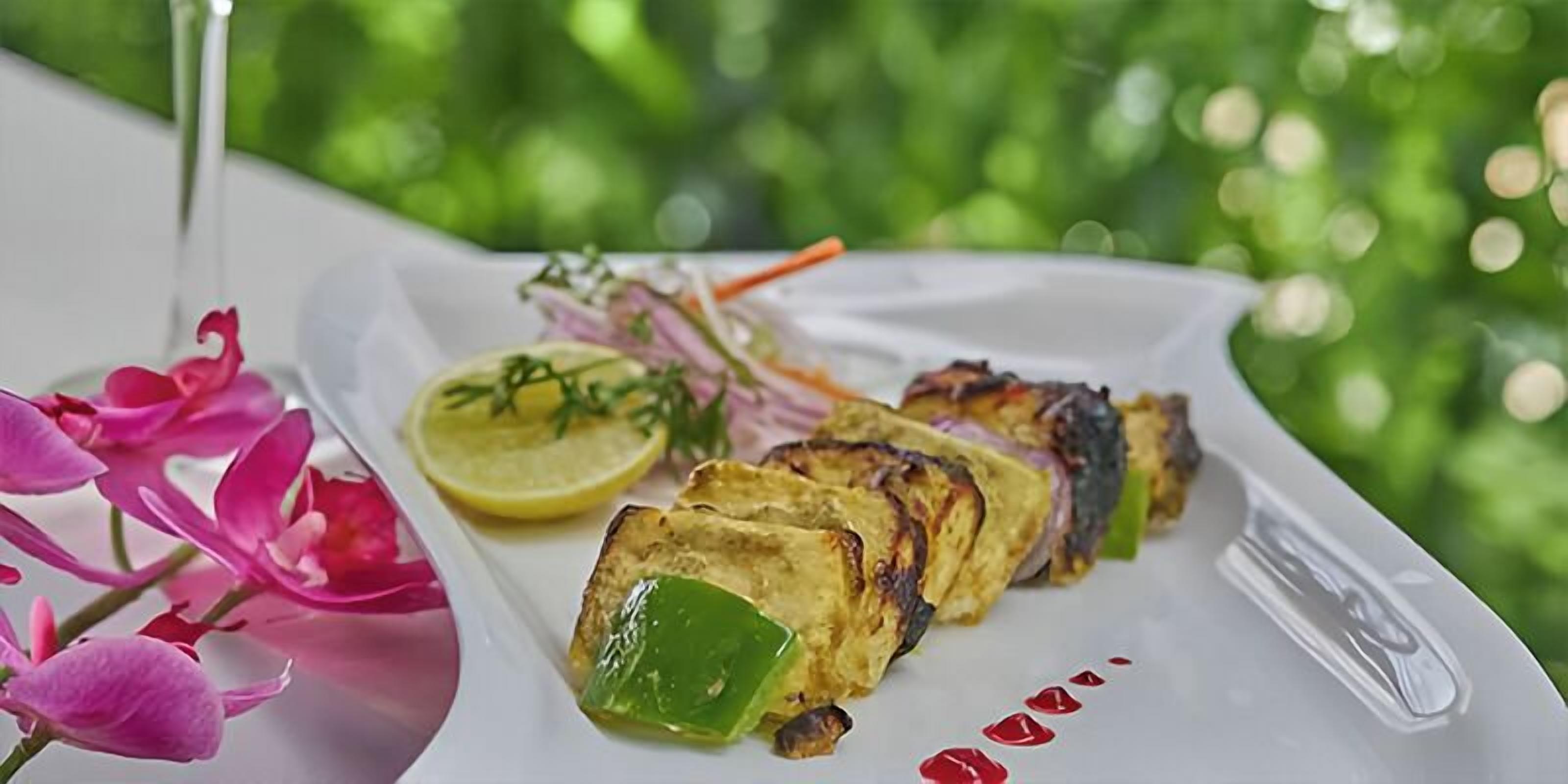 A plate of grilled chicken with lemon and herbs, accompanied by pink flowers.