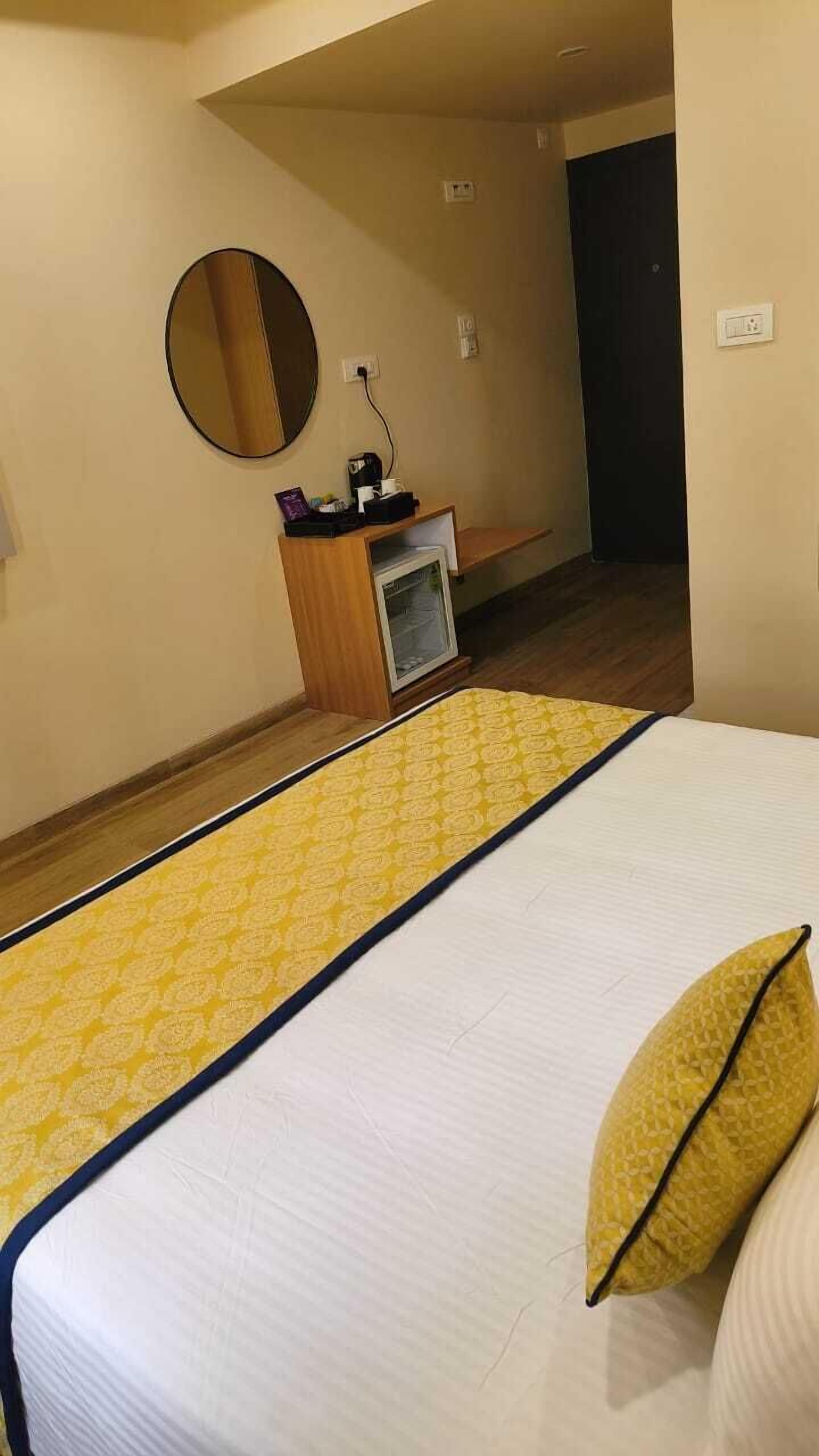 Ein Hotelzimmer mit einem Bett, einem Nachttisch, einem Spiegel und einem kleinen Schreibtisch mit Computer und Tasse.