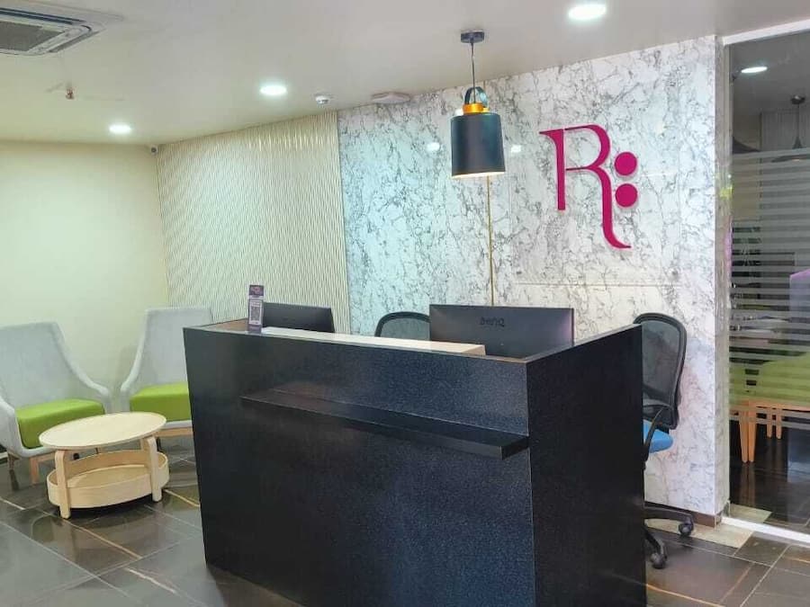Un área de recepción con pared de mármol, mostrador negro y sillones tapizados en tono verde.
