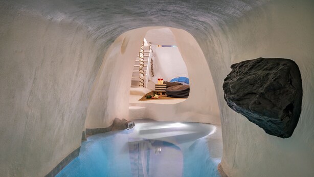 An ice hotel interior with a clear blue pool, a wooden bench, and a large rock feature. - Mystagoge Retreat with subterranean pool/jacuzzi (Vothonas)
