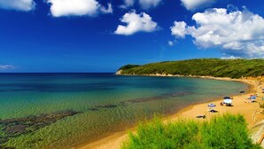 A beach with clear turquoise water, a sandy shore, and a line of umbrellas. - House by the sea, 2 km from Baratti gulf & Etruscan archaeological park (Stazione di Populonia)