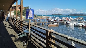 A wooden pier with a sign for boat rental, boats docked in the water, and a clear view of the sea and distant hills. - House by the sea, 2 km from Baratti gulf & Etruscan archaeological park (Stazione di Populonia)