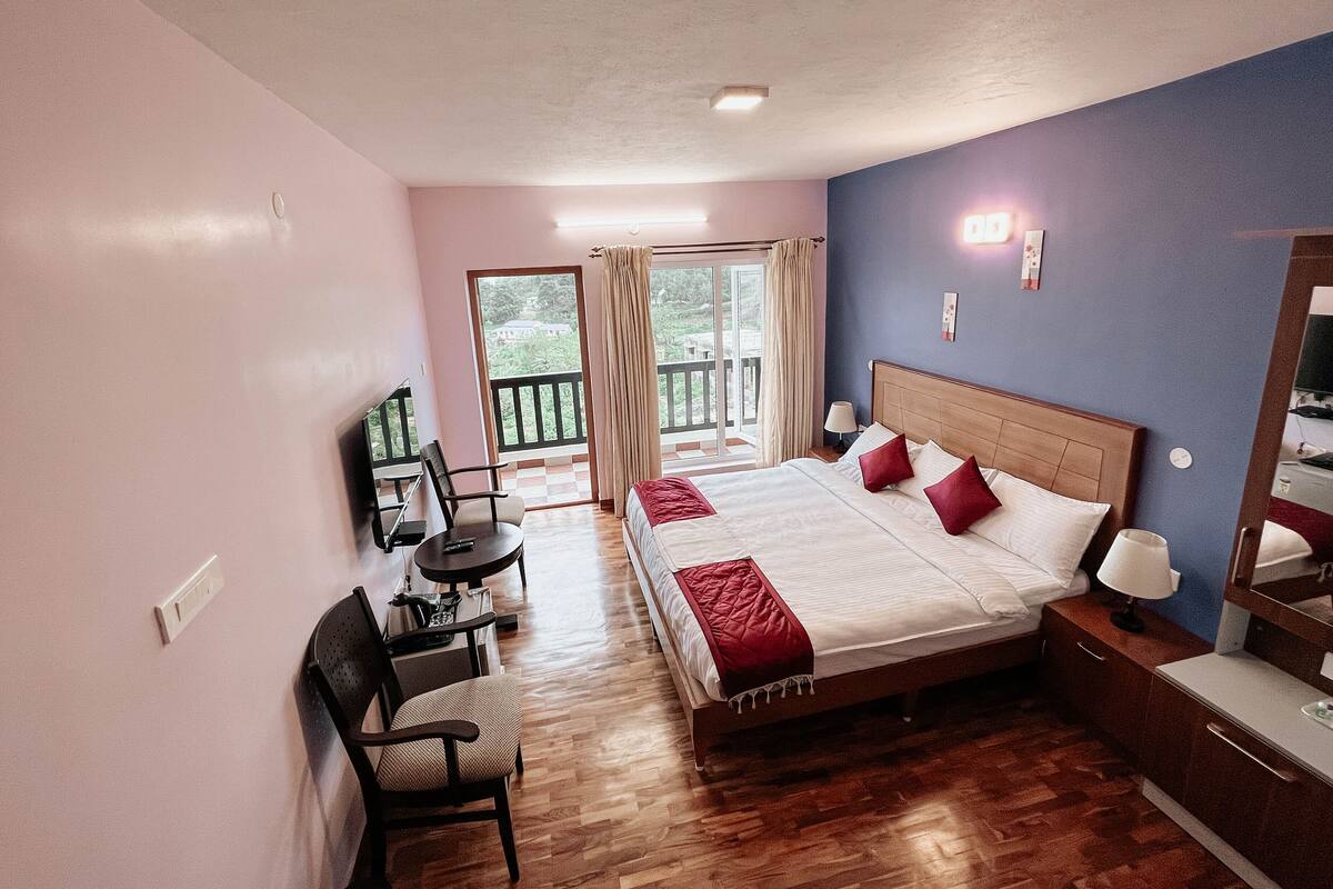 A hotel room with a bed, a desk, a chair, a TV, and a balcony with curtains.