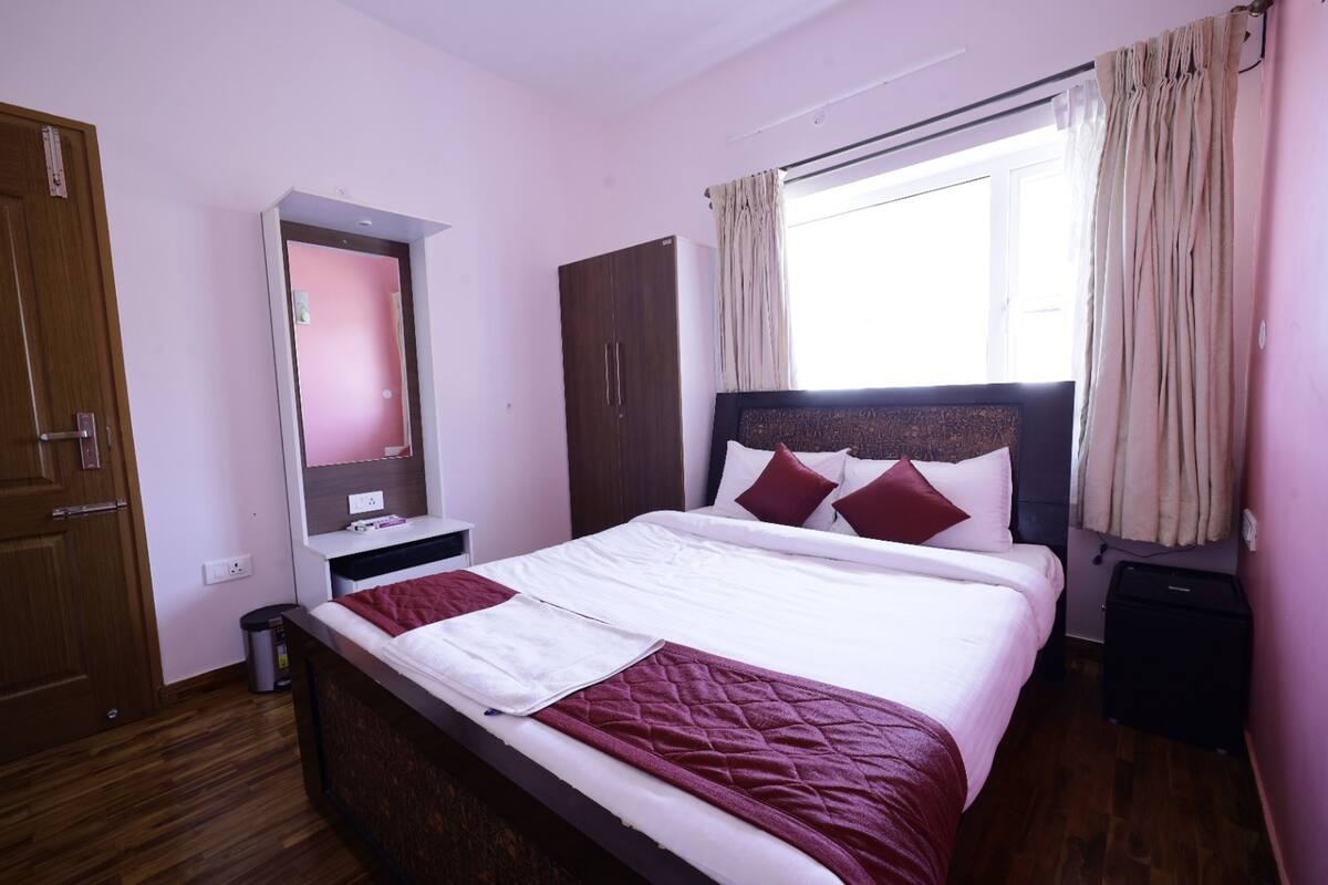 A neatly arranged bedroom with a bed, a wardrobe, a mirror, and a window with curtains.