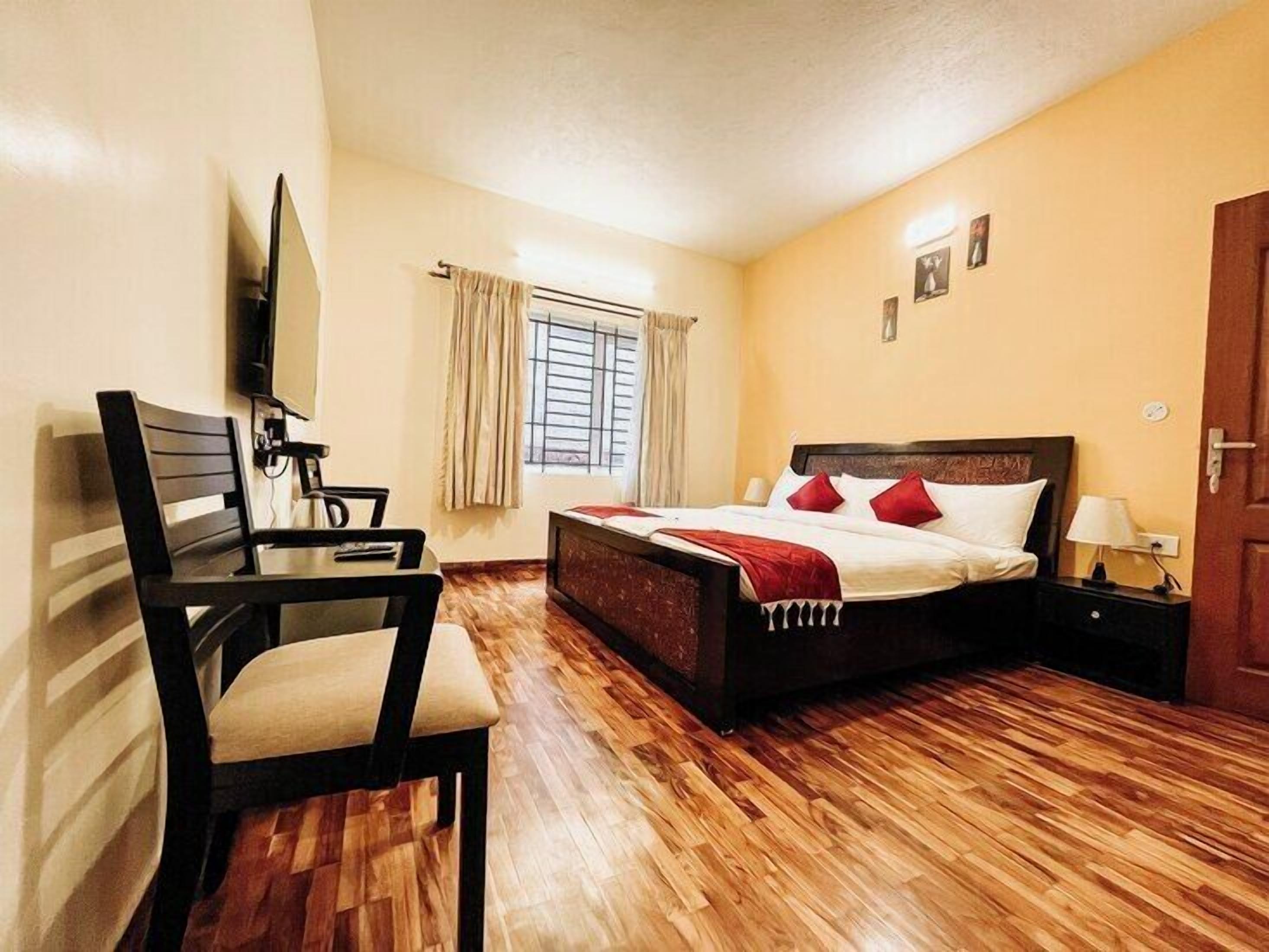 Quarto de hotel com cama, escrivaninha, cadeira, televisão e janela com cortinas.