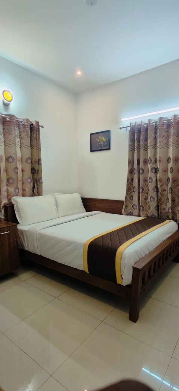 A neatly made bed with a wooden frame, a bedside table, and curtains with a pattern. - Purple Orchid By Xacro Xperiences (Kodaikanal)