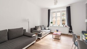 Ein modernes Wohnzimmer mit einem grauen Sofa, einem kleinen Couchtisch und einem Essbereich mit einem Glastisch und Stühlen.