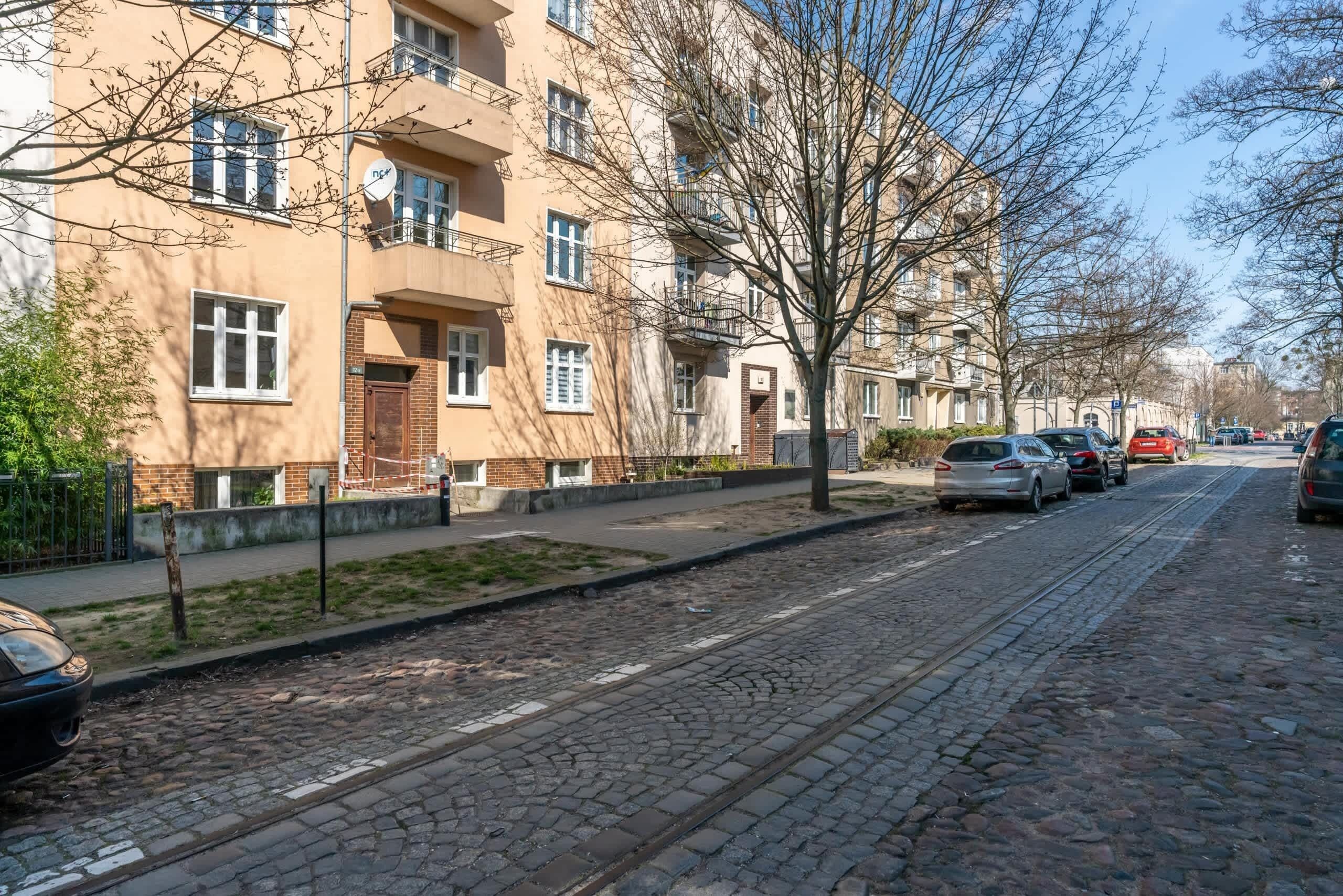 Una strada residenziale con palazzi, un binario del tram e auto parcheggiate.