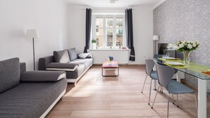 Ein modernes Wohnzimmer mit einem grauen Sofa, einem Glastisch und Blick auf die Stadt durch große Fenster.