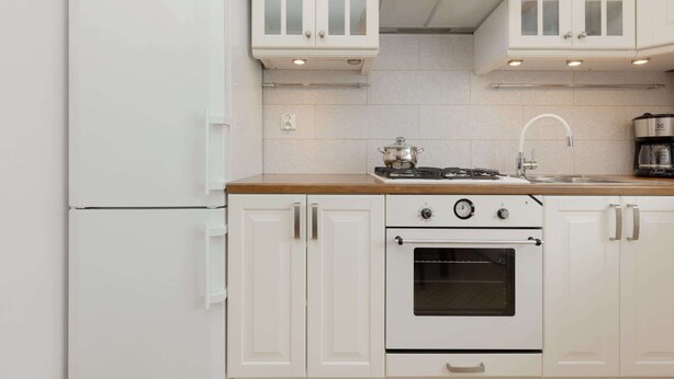 Una cocina con armarios blancos, estufa, horno y cafetera.