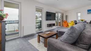 Un salon moderne avec un canapé gris, une table basse en bois et un téléviseur à écran plat fixé au mur.