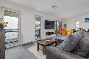 Ein modernes Wohnzimmer mit einem grauen Sofa, einem Holztisch und einem flachbildfernseher, der an der Wand montiert ist.