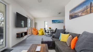 Ein modernes Wohnzimmer mit grauem Sofa, Couchtisch aus Holz und einem flachbildfernseher an der Wand.
