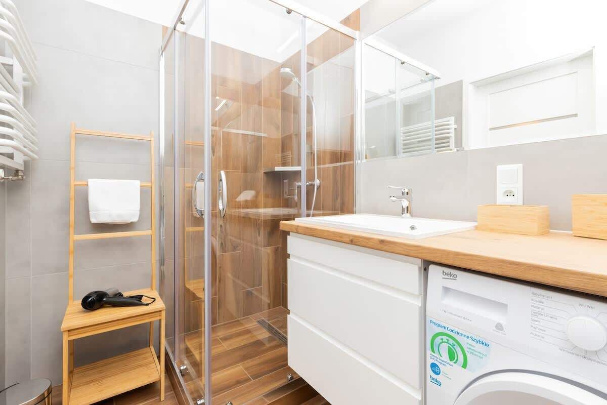 A modern bathroom with a glass shower enclosure, a wooden vanity, and a built-in washing machine.