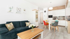 Un salon moderne avec un canapé vert foncé, une table basse en bois et un coin repas comprenant une table blanche et des chaises colorées.