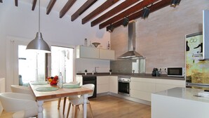 Une cuisine moderne avec un plancher en bois, des meubles blancs, un four encastré et un coin repas comprenant une table en bois et des chaises blanches.