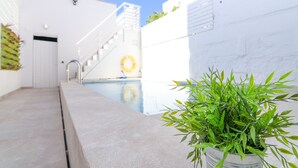 Un espace piscine avec un chemin en béton, un mur blanc et un escalier.