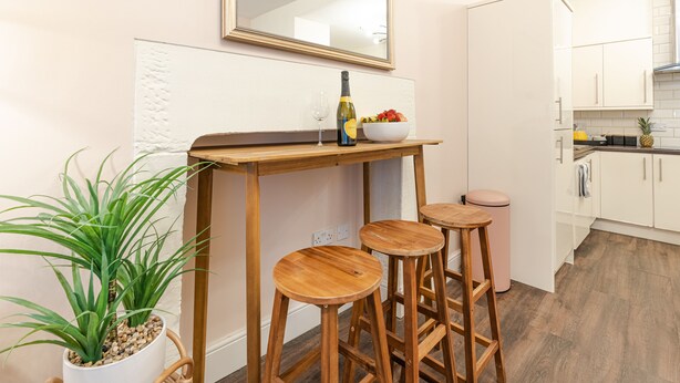A kitchen with a wooden table, stools, a bowl of fruit, a bottle, and a potted plant. - Bloomfield 1 (Lancaster)