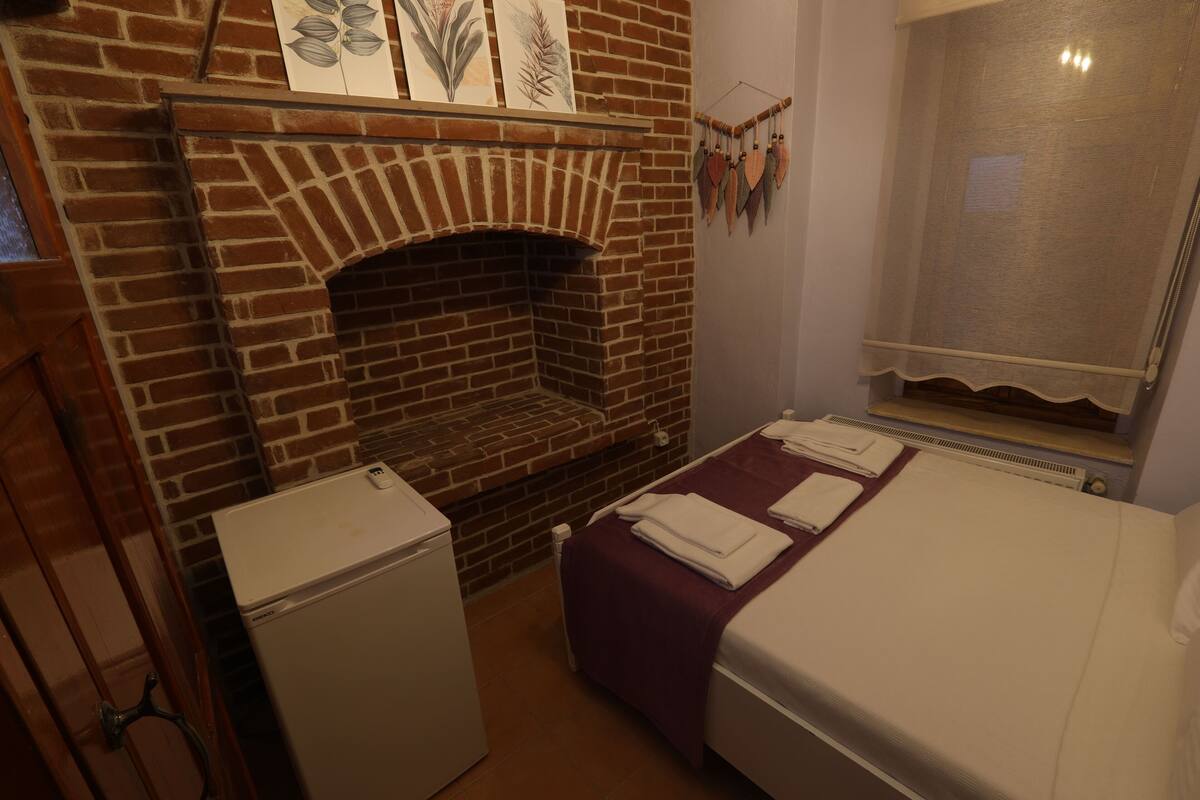 Una habitación con chimenea de ladrillo, cama con colcha morada y radiador blanco.