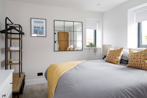 Une chambre à coucher avec un lit, un miroir, un tableau encadré, une fenêtre et une table de chevet.