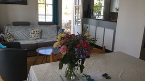 A living room with a sofa, a dining table with a vase of flowers, and a kitchen area in the background. - Comfortable apartment with harbor view (Arzon)