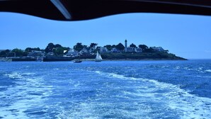 A coastal view with a sailboat, a lighthouse, and houses on a small island. - Comfortable apartment with harbor view (Arzon)