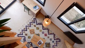 Ein Zimmer mit Holzboden, einem bunten Teppich, einem Tisch mit einem Buch und einer hängenden Leuchte.