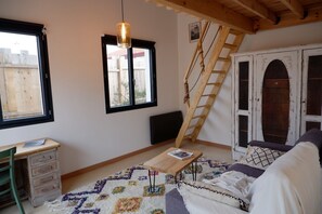 A cozy room with a wooden ladder, a small table with a magazine, a colorful rug, and a sofa with a white blanket.