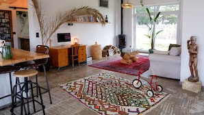 Ein gemütliches Wohnzimmer mit einem Holztisch, einem Computer, einem Bücherregal, einem großen Fenster und einem roten Teppich mit Muster.