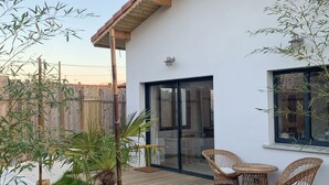Eine moderne Terrasse mit Korbmöbeln, einem Holzboden und einem weißen Gebäude mit einem Ziegeldach.