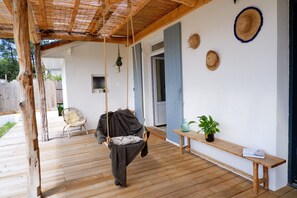 A wooden deck with a hanging swing, a bench, and a potted plant.