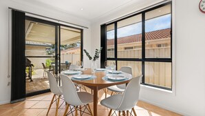 Un coin repas avec une table dressée pour quatre personnes, de grandes fenêtres et une vue sur le jardin.