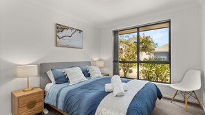 Une chambre moderne avec une grande fenêtre, un lit avec une literie bleue, une table de chevet avec une lampe et une chaise.