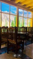 Uma área de refeições com mesa e cadeiras, janelas amplas com vista para as montanhas e teto de madeira.