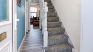 A staircase with a white balustrade leading to a living room area with a couch and a window. - The Beach House (Mablethorpe)