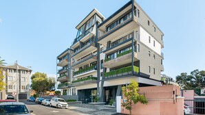A multi-story building with balconies, a parking area, and a clear sky. - TenOnQ B4 (Cape Town)