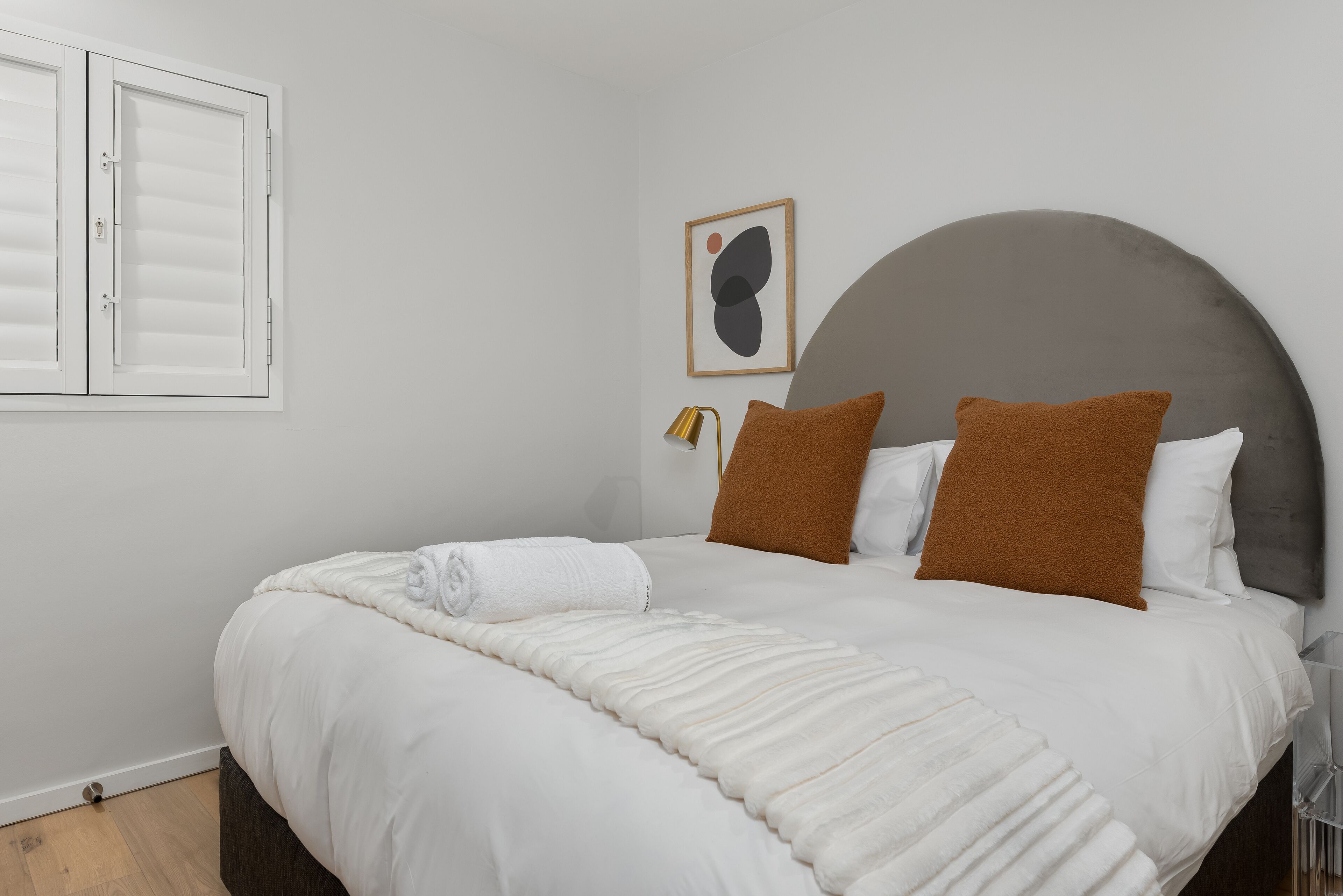 A neatly made bed with a white duvet, two brown pillows, and a white towel rolled up at the foot.