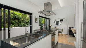 A modern kitchen with a large island, stainless steel appliances, and a view of greenery outside. - TenOnQ B4 (Cape Town)