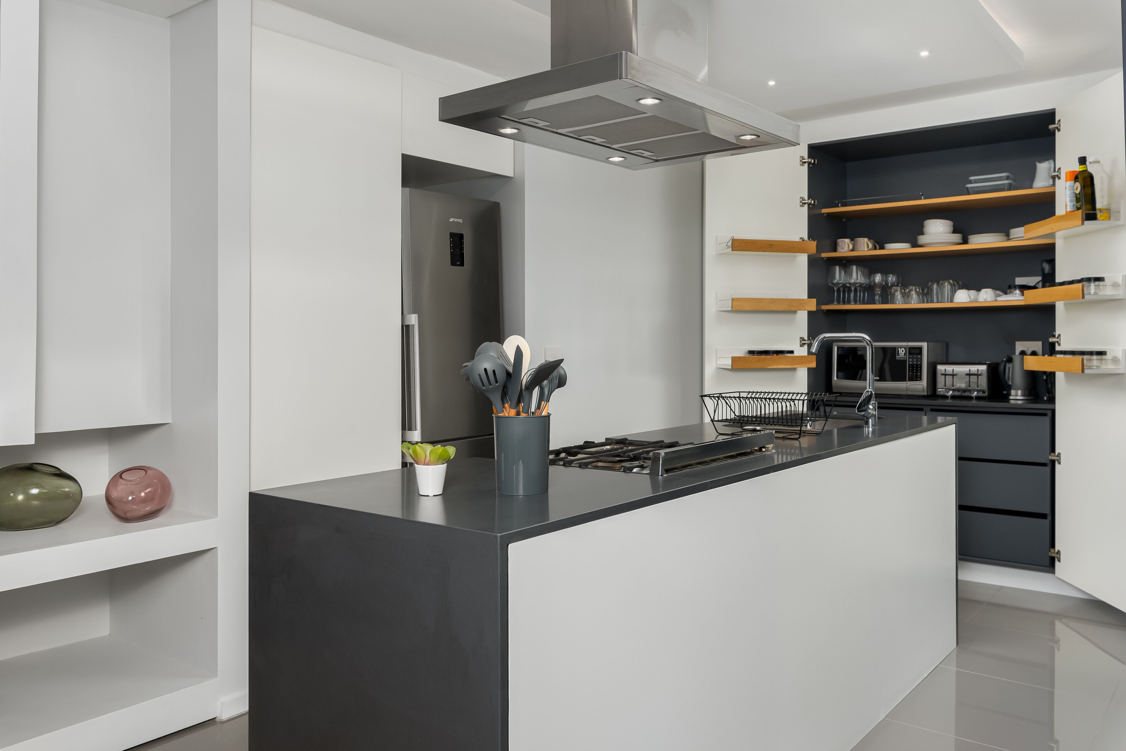 A modern kitchen with a central island, built-in appliances, and open shelving.