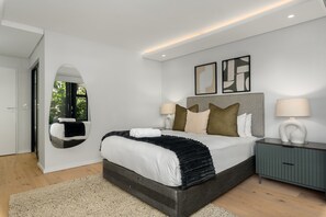 A modern bedroom with a large bed, two bedside tables, a mirror, and abstract wall art.