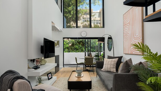 A modern living room with a sofa, coffee table, and a TV. There is a dining area with chairs and a table. A large window offers a view of greenery outside. - TenOnQ B4 (Cape Town)