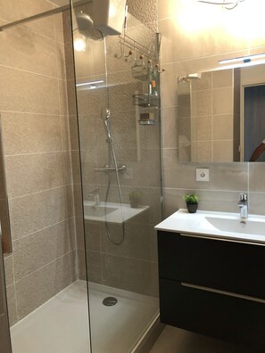 Et moderne badeværelse med en brusekabine i glas, en hvid vask og et spejl over vasken.