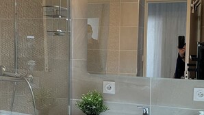 Un baño moderno con ducha de vidrio, lavamanos blanco y un espejo grande.